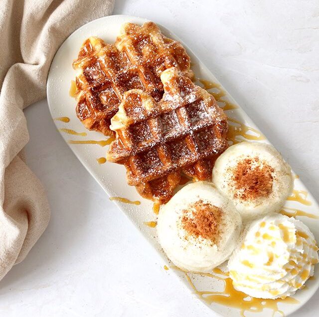 Waffle caldi su vassoio bianco e sfondo bianco con palline di gelato vaniglia come accompagnamento